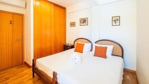 Una habitación de hotel con un armario de madera, una cama con ropa de cama blanca y naranja, y dos cuadros en la pared.