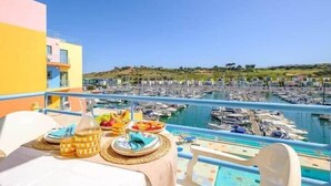 Un balcón con una mesa dispuesta para el desayuno, con vistas a un puerto deportivo lleno de barcos.