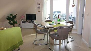 A dining area with a table and chairs, a television, and a plant.
