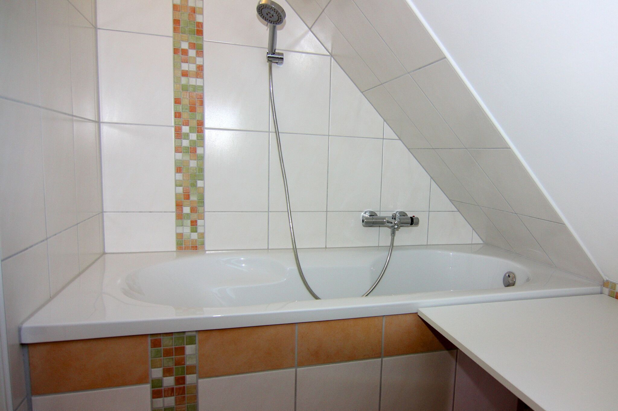 A bathroom with a bathtub, a showerhead, and a tiled wall.