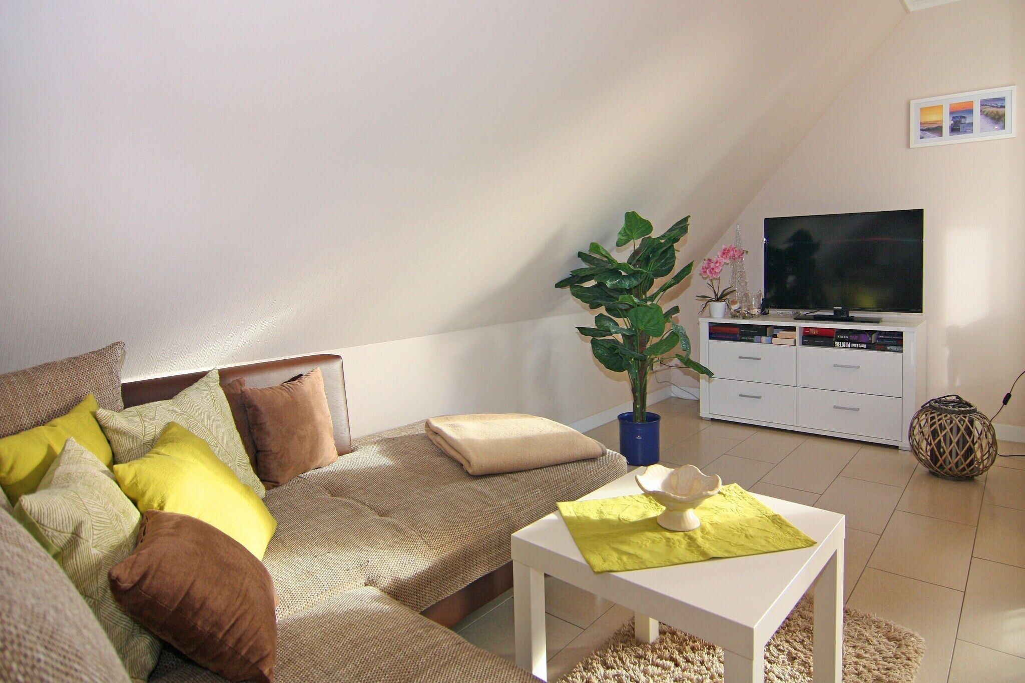 Ein gemütliches Wohnzimmer mit einer Couch, einem Couchtisch, einem Fernseher und einer Pflanze.