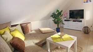 A cozy living room with a sofa, a coffee table, a TV, and a plant. - Appartementhaus Strandloper, Zinnowitz (Zinnowitz)