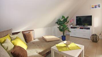 Ein gemütliches Wohnzimmer mit einer Couch, einem Couchtisch, einem Fernseher und einer Pflanze.