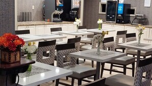 Un restaurant avec plusieurs tables et chaises, un appareil à café et un réfrigérateur à l’arrière-plan.
