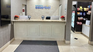 Un espace d’accueil avec un comptoir, un téléviseur fixé au mur, un panneau indiquant « SONESTA essential », et un présentoir de collations.