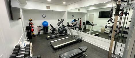 A gym with treadmills, a bench, dumbbells, a stationary bike, and a mirror.