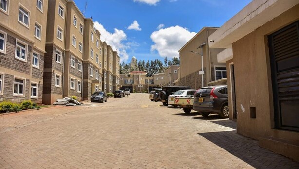 A multi-story residential building with a paved driveway and parked vehicles.