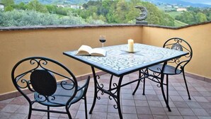 A table with a book and a glass of red wine, two chairs, and a candle on a balcony with a view of a green landscape. - Villa in Vinci with Pool & Panoramic Views (Lamporecchio)