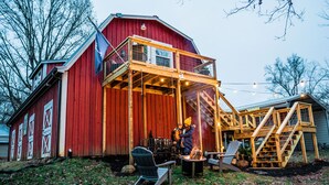 A red barn with a wooden deck and a staircase leading to a second level.