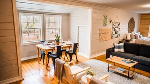 A spacious living room with a black sofa, wooden coffee table, and a dining area with a table and chairs.