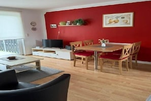 A living room with a dining area, a TV, and a red wall.