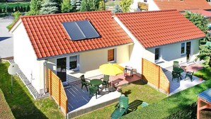 Ein zweistöckiges Haus mit rotem Ziegeldach, einer Solaranlage, einer Terrasse mit Gartenmöbeln und einem Holzzaun.