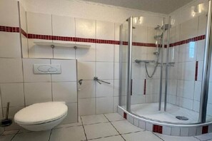 A bathroom with a toilet, a shower with a glass door, and tiled walls.