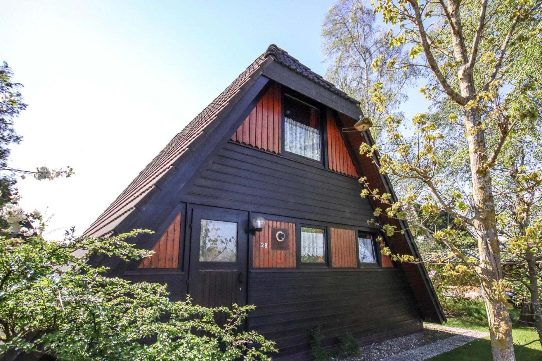 Ein zweistöckiges Holzhaus mit einem steilen Satteldach, einer Haustür und zwei Fenstern im Obergeschoss.