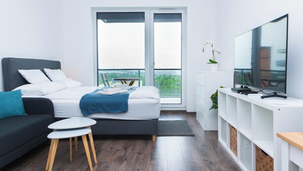A modern bedroom with a bed, a sofa, a TV, and a balcony with a city view. -  WaterFront City Apartments by FirstHost (Budapest)