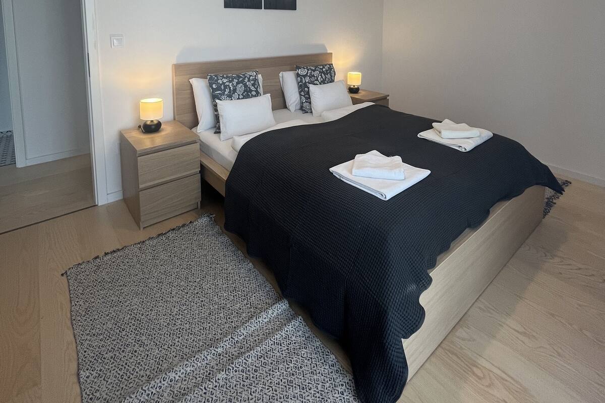 A bedroom with a bed, bedside tables, a nightstand, a rug, and a ceiling light fixture.