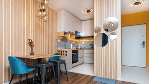A modern kitchen with wooden accents, a dining area with blue chairs, and a small TV. -  WaterFront City Apartments by FirstHost (Budapest)