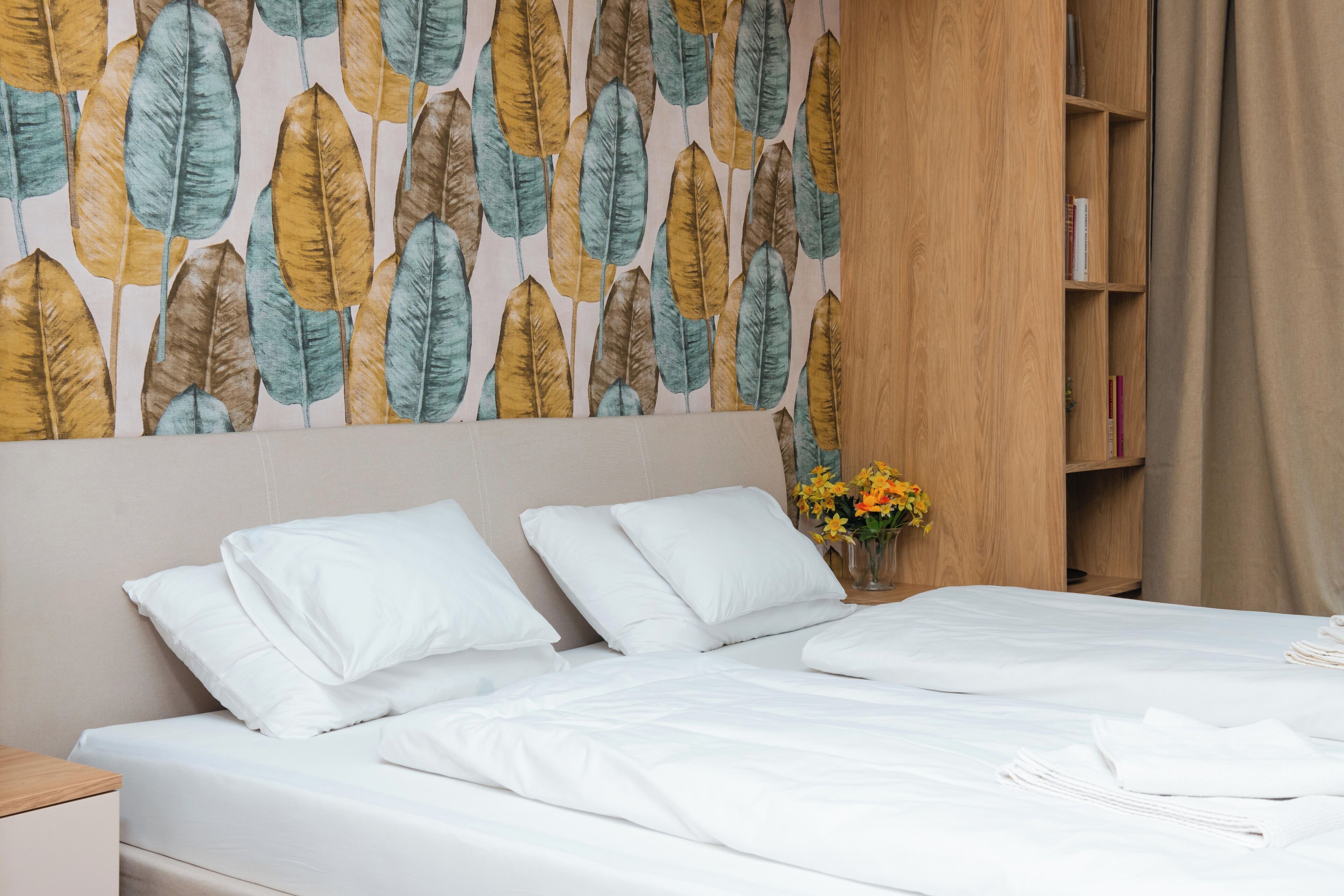 Ein ordentlich bezogenes Bett mit weißen Leinen, einem Holz-Kopfteil und einer Wand mit einem Blattmuster.