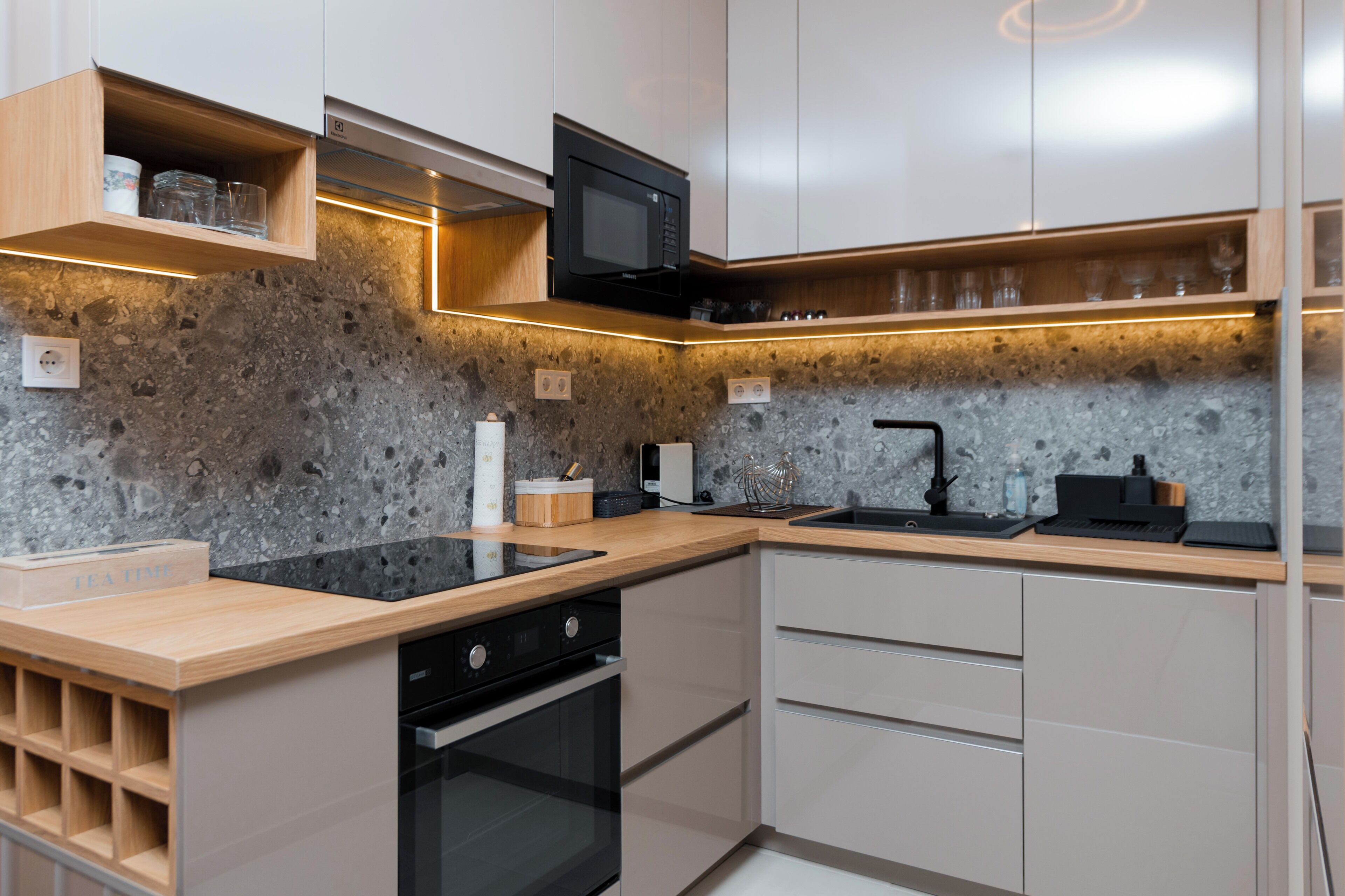 A modern kitchen with a granite countertop, built-in oven, and wooden shelves.
