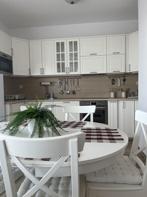 A modern kitchen with white cabinetry, a dining table with chairs, and a hanging utensil rack. -  WaterFront City Apartments by FirstHost (Budapest)