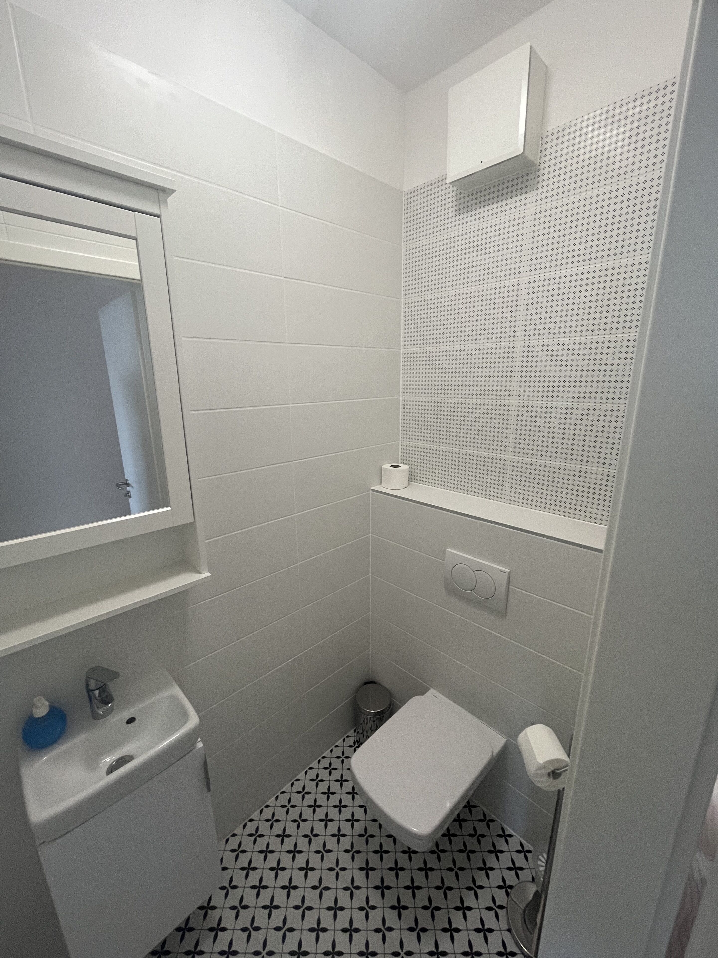 Een kleine, praktische badkamer met witte tegels, een wastafel, een toilet en een spiegel.