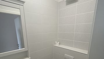 Een kleine, praktische badkamer met witte tegels, een wastafel, een toilet en een spiegel.