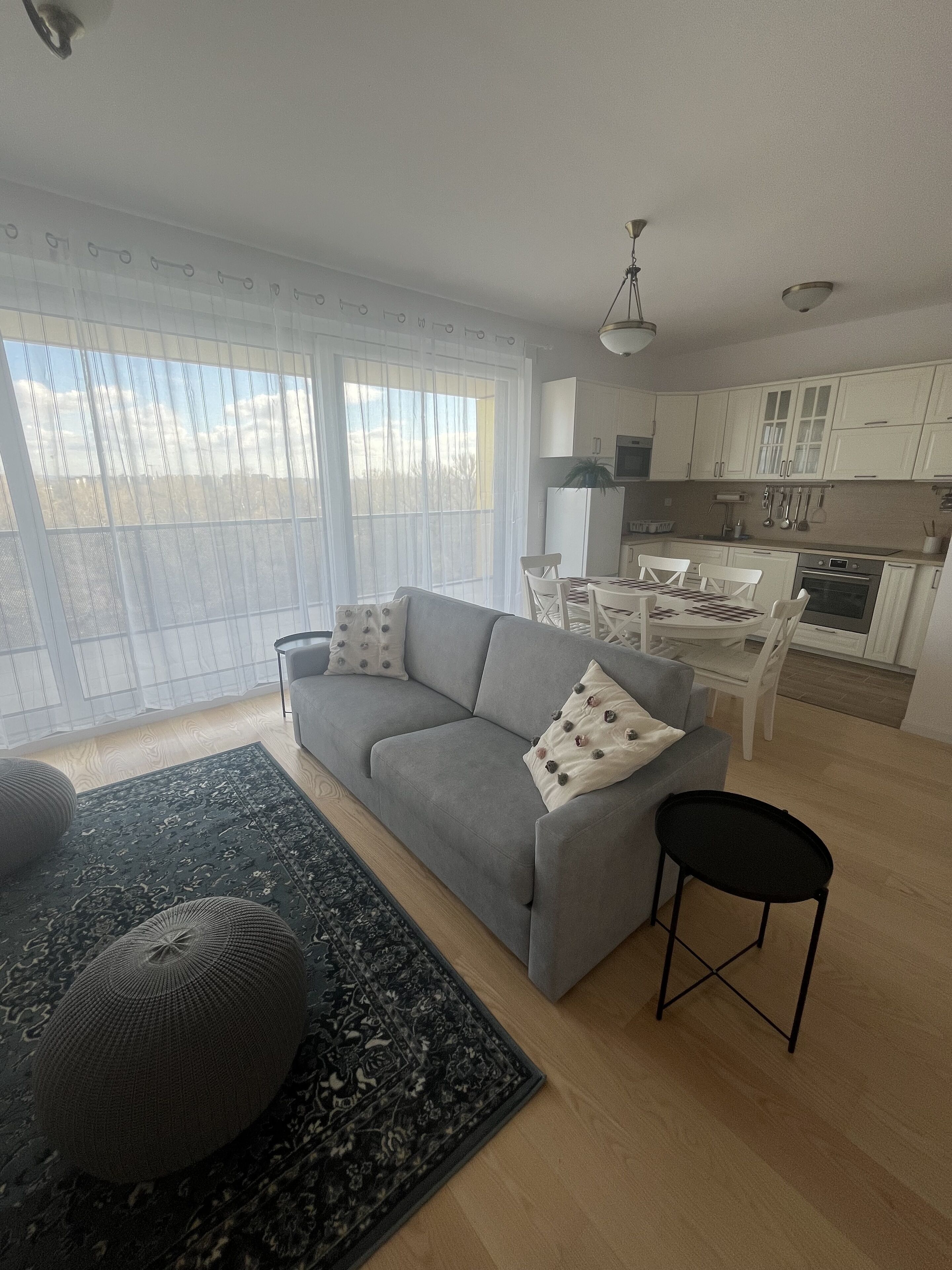 A modern living room with a grey sofa, a black ottoman, and a patterned rug.