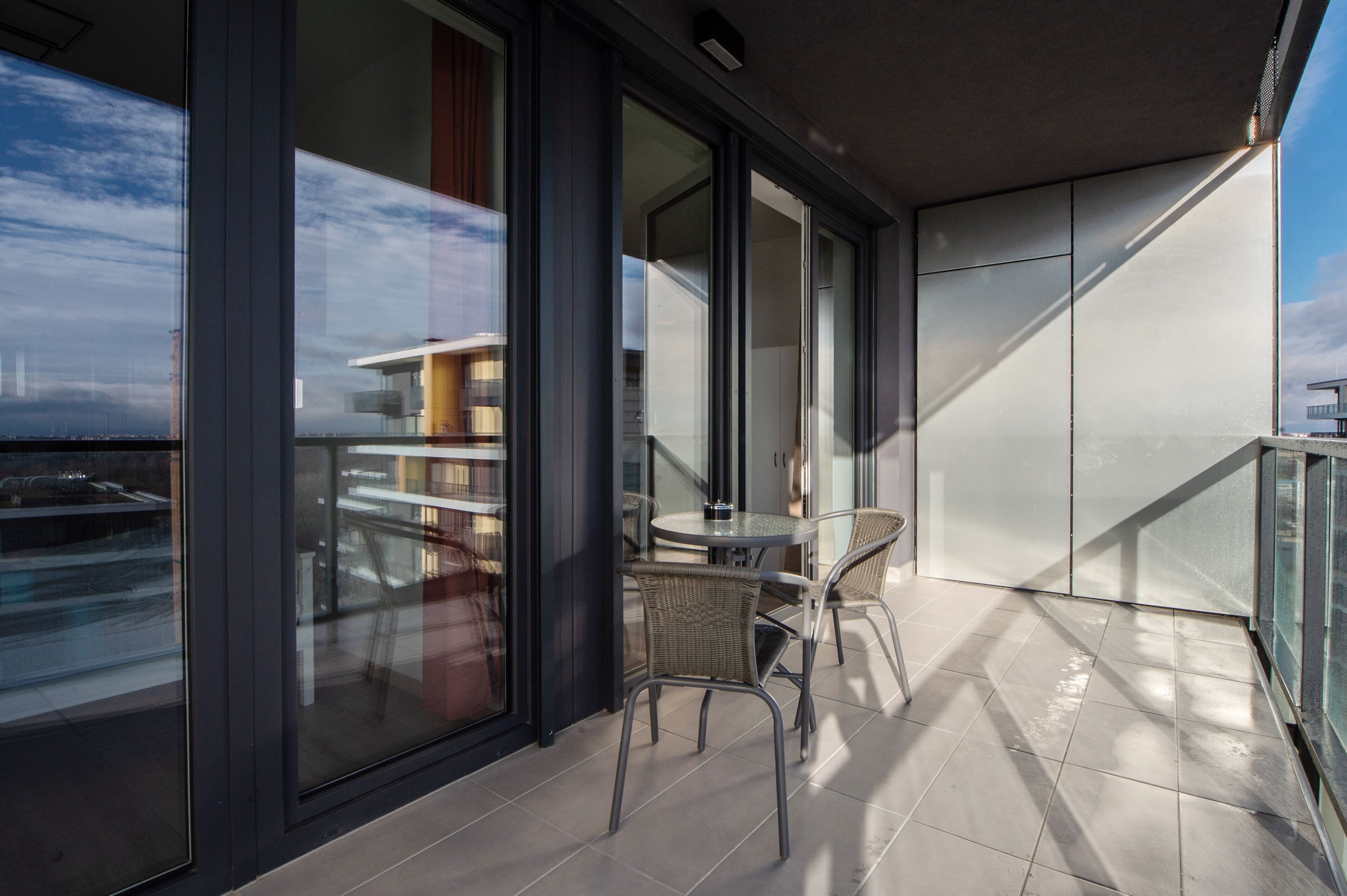 A modern balcony with a glass door, a round table, and wicker chairs.