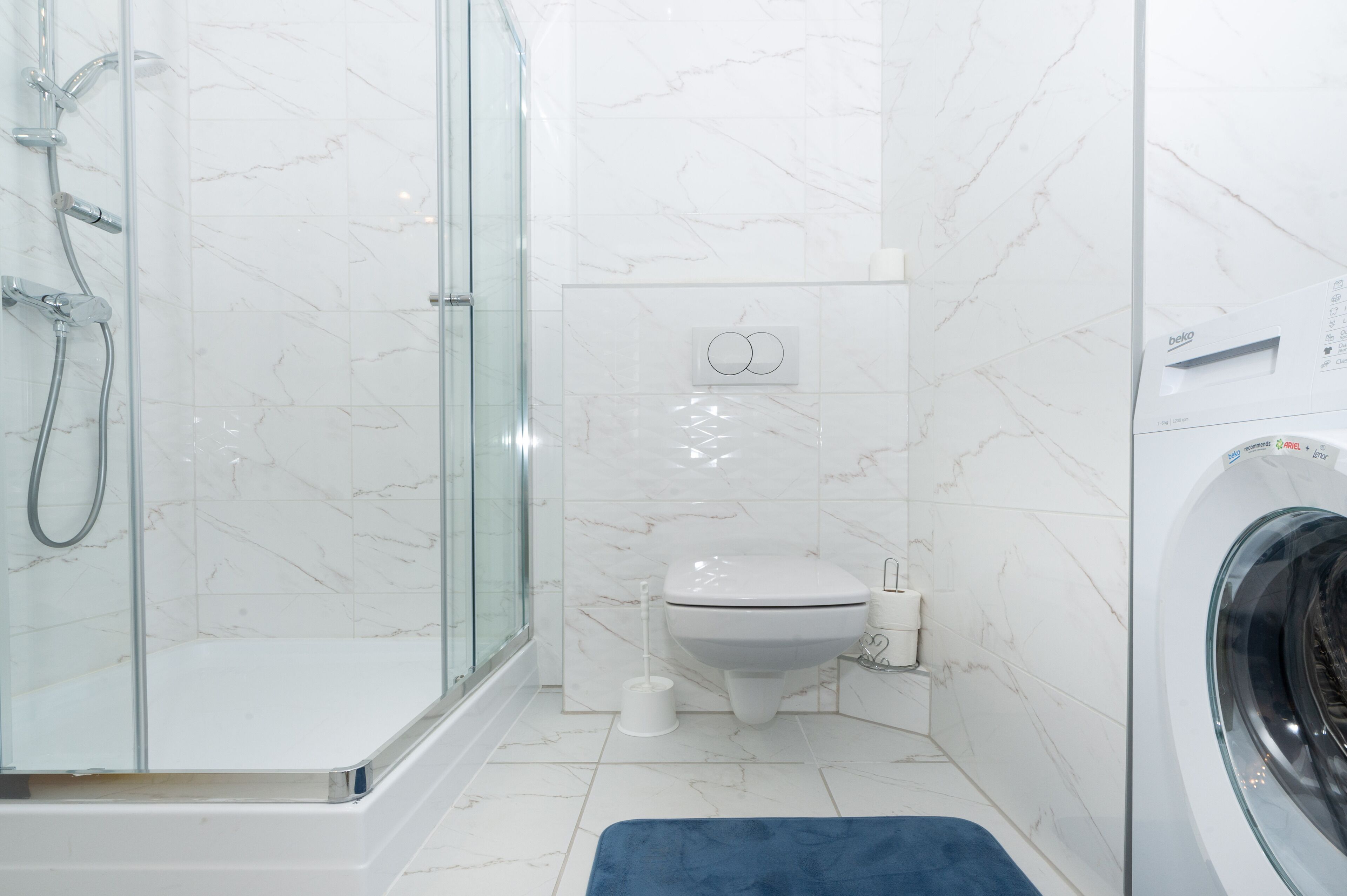 A bathroom with a glass shower enclosure, a toilet, and a washing machine.