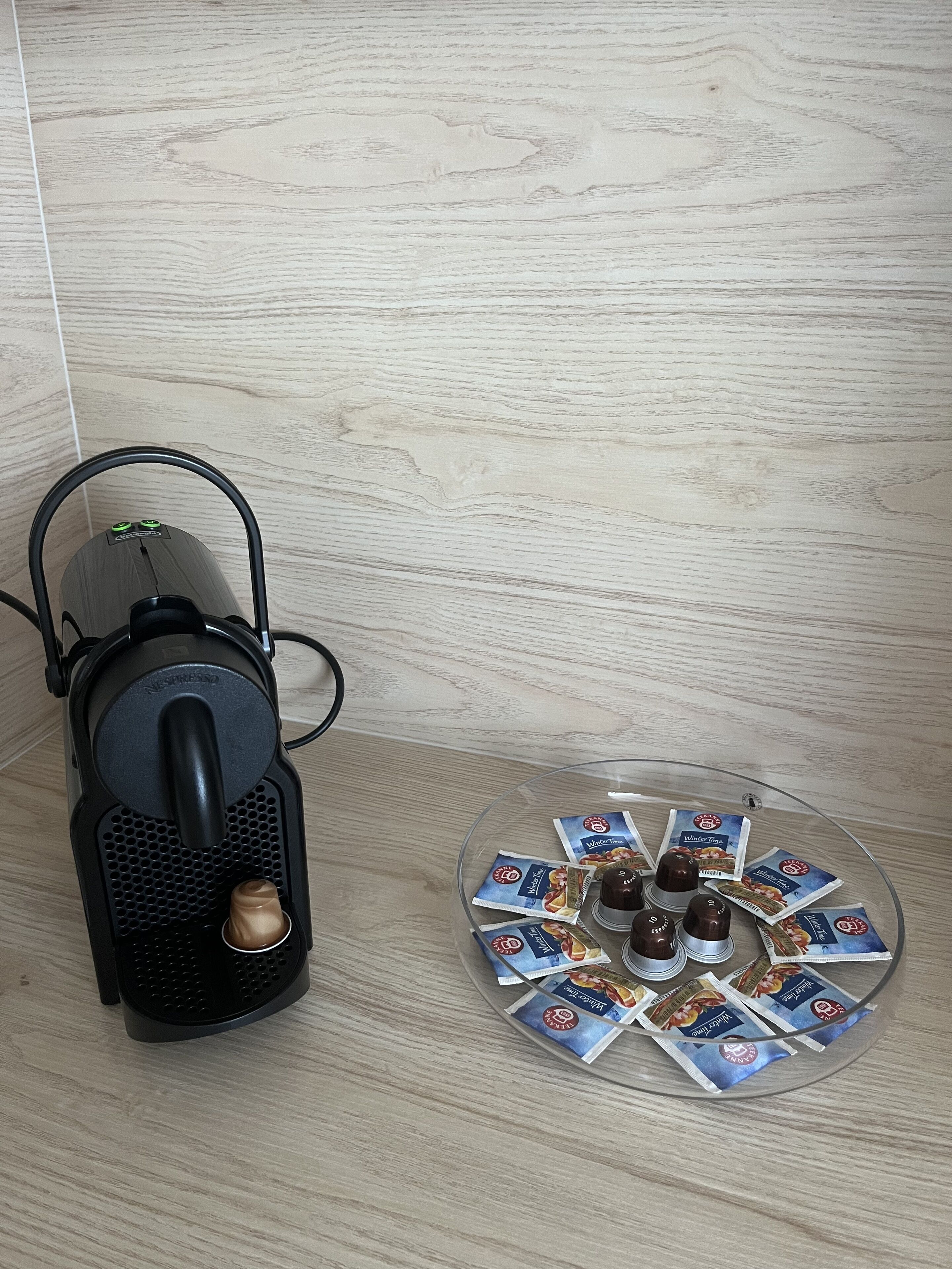 Una macchina Nespresso e un vassoio di vetro con diverse cialde per caffè.