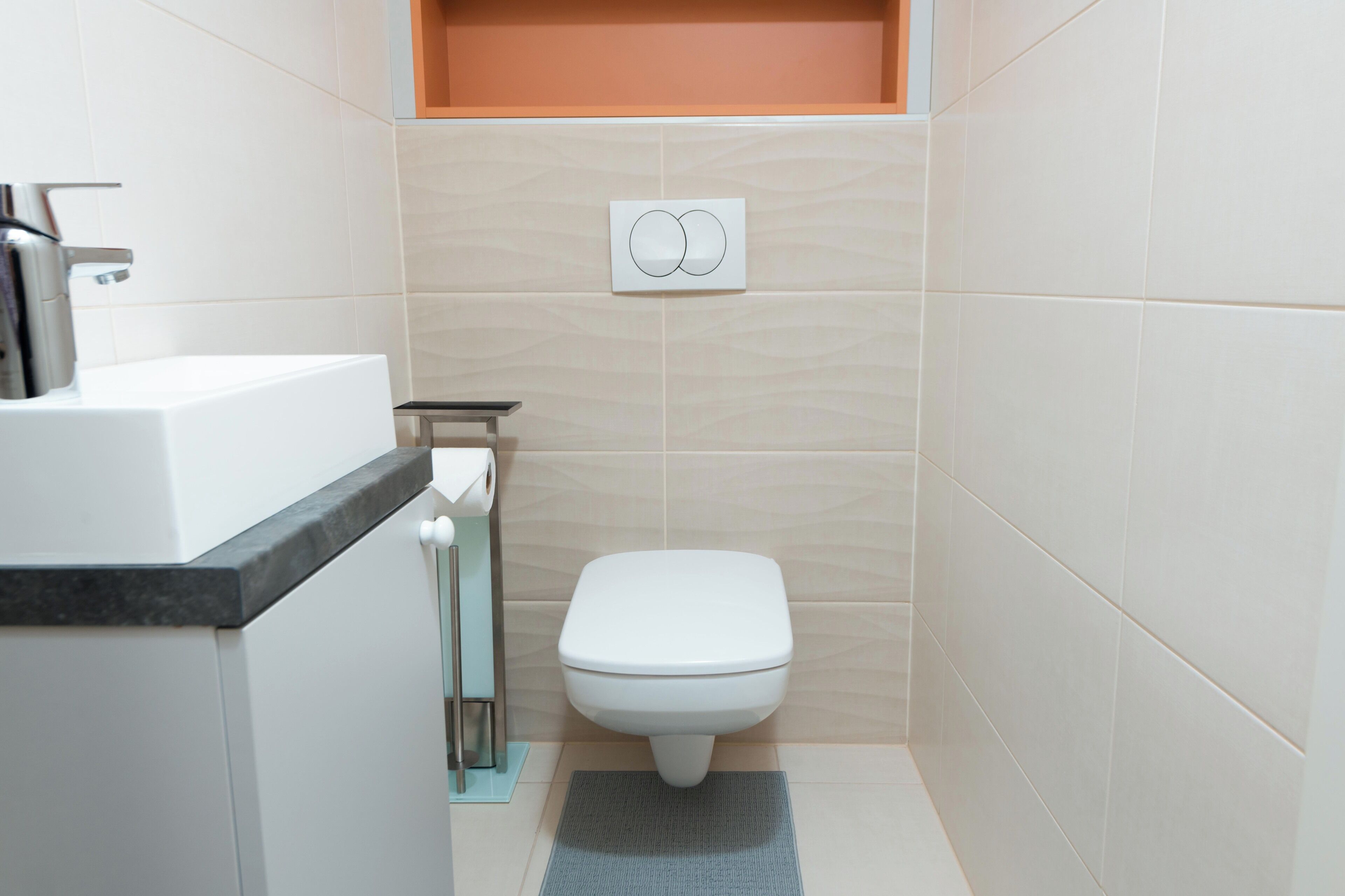 Et lille, moderne badeværelse med et hvidt toilet, en vask med sort bordplade og en håndklædestang.