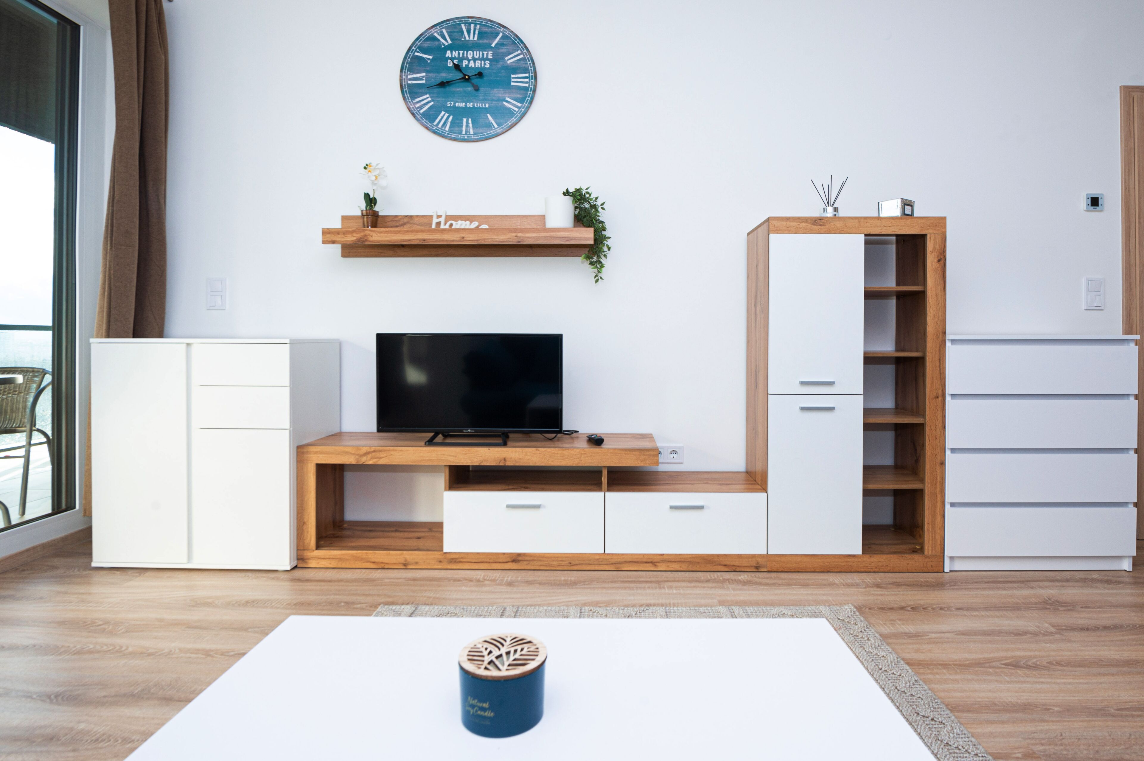 Un soggiorno moderno con televisione a schermo piatto, mobile TV in legno, pensili bianchi e un orologio a parete.