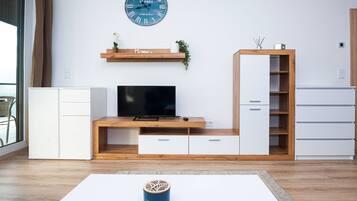 Un soggiorno moderno con televisione a schermo piatto, mobile TV in legno, pensili bianchi e un orologio a parete.