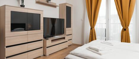 Una habitación de hotel moderna con una cama, televisión, armario y ventana con cortinas.