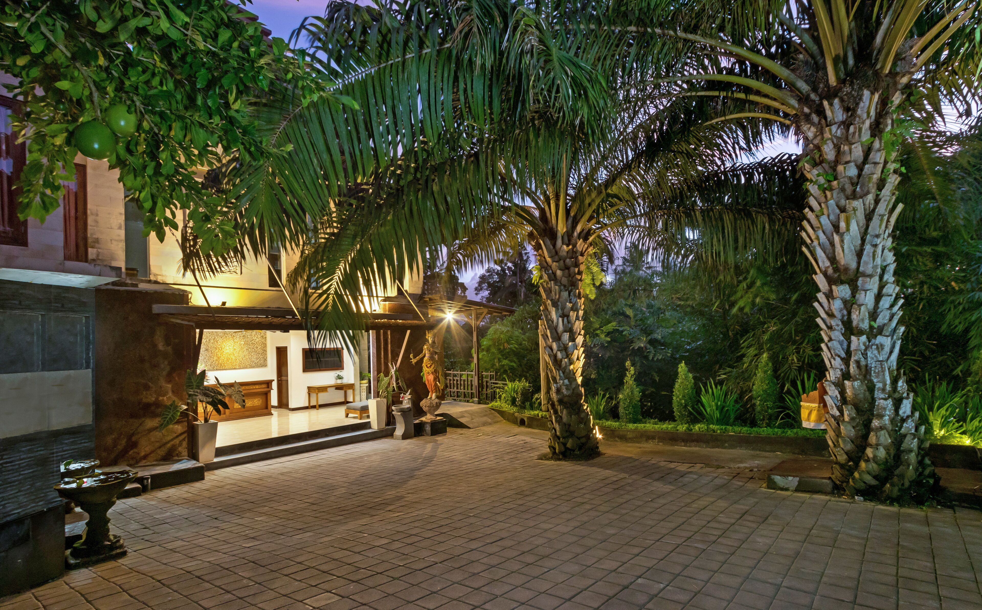 A courtyard with a stone fountain, palm trees, and a building with a covered area.
