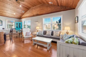 Un salon spacieux doté d’un parquet en bois, d’une table basse blanche, d’un canapé gris agrémenté de coussins à motifs et d’une armoire bleue.