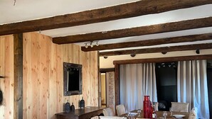A dining area with a wooden table and chairs, a television mounted on the wall, and a fireplace in the background. - Gite in Cévennes (Saint-Christol-lès-Alès)