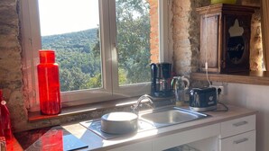 A kitchen with a window, a sink, a stove, and a cabinet with glassware. - Gite in Cévennes (Saint-Christol-lès-Alès)