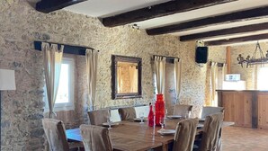A dining area with a stone wall, wooden beams, and a tiled floor. - Gite in Cévennes (Saint-Christol-lès-Alès)