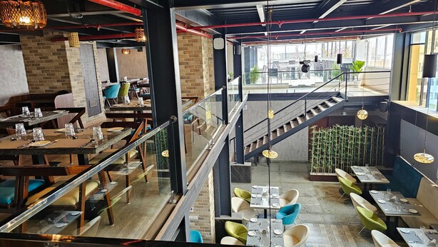 A modern restaurant with a mezzanine level, exposed brick walls, and a variety of seating options including tables and chairs. - Quality Inn Rockwell Grand, Bangalore (Bengaluru)