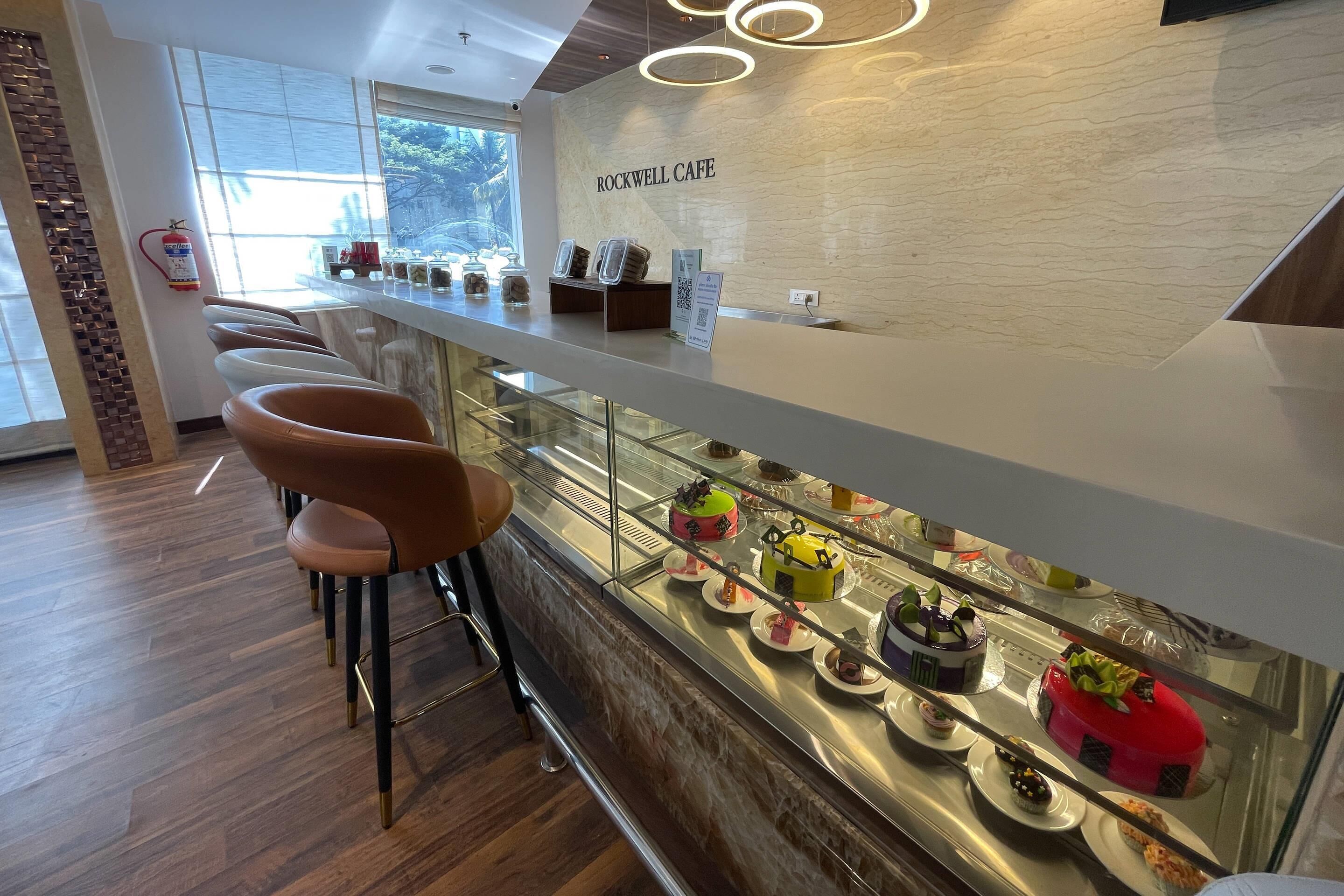 A modern interior with a bar area, bar stools, and a display case with various desserts.