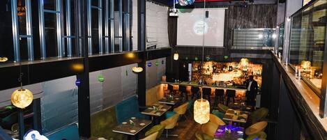 A restaurant with multiple dining areas, a bar, and a projection screen displaying 'Annual Cricket Live'.