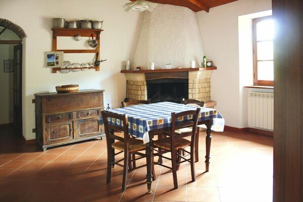 Un coin repas avec une nappe à carreaux, des chaises en bois, une cheminée et un sol carrelé.