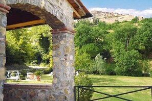 Une construction en pierre offrant une vue sur un paysage verdoyant et luxuriant, ainsi que sur une colline lointaine parsemée de bâtiments.