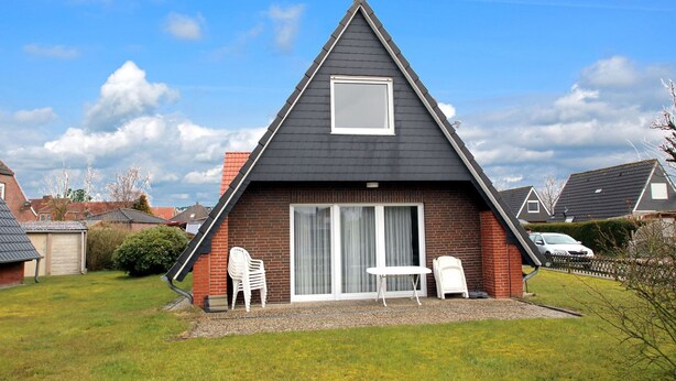 A house with a black roof, a large sliding glass door, and a small patio with two white chairs and a table. - Greetjehaus mit Garten, Nähe Strand, Dornumersiel (Dornumersiel)