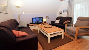 A modern living room with a brown sofa, a wooden coffee table, and a TV on a stand. - Greetjehaus mit Garten, Nähe Strand, Dornumersiel (Dornumersiel)