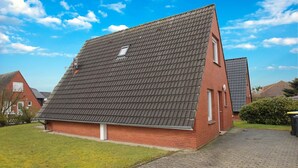 A red brick house with a steeply pitched roof, a small window, and a paved driveway. - Greetjehaus mit Garten, Nähe Strand, Dornumersiel (Dornumersiel)