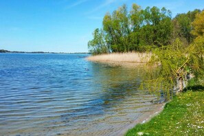 A calm lake with clear water, surrounded by grassy areas and trees.