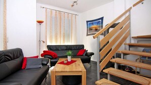A modern living room with a black leather sofa, a wooden coffee table, and a staircase with wooden steps. - Doppelhaushaelfte am Hafen von Neuendorf (Neuendorf)