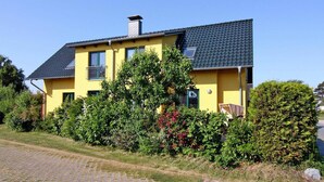 A yellow house with a dark roof, surrounded by greenery and a paved driveway. - Doppelhaushaelfte am Hafen von Neuendorf (Neuendorf)